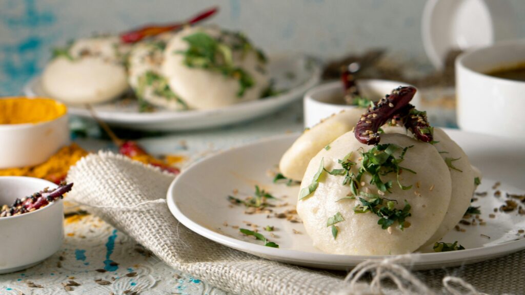 Capture of South Indian idli garnished with fresh herbs and spices, evoking a rich culinary experience.