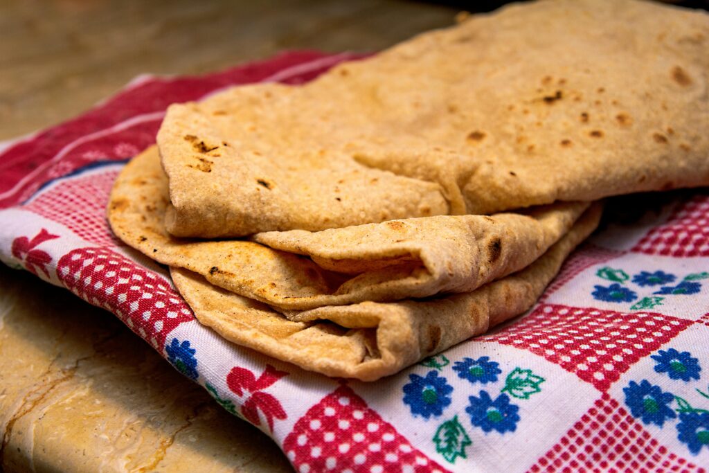 Freshly made chapati placed on a vibrant patterned cloth, highlighting its texture and homemade appeal.